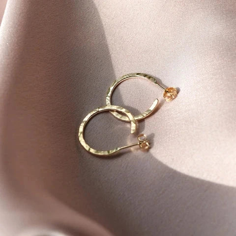9ct solid solid gold hoop earrings laying in sunlight on a pale pink silk background