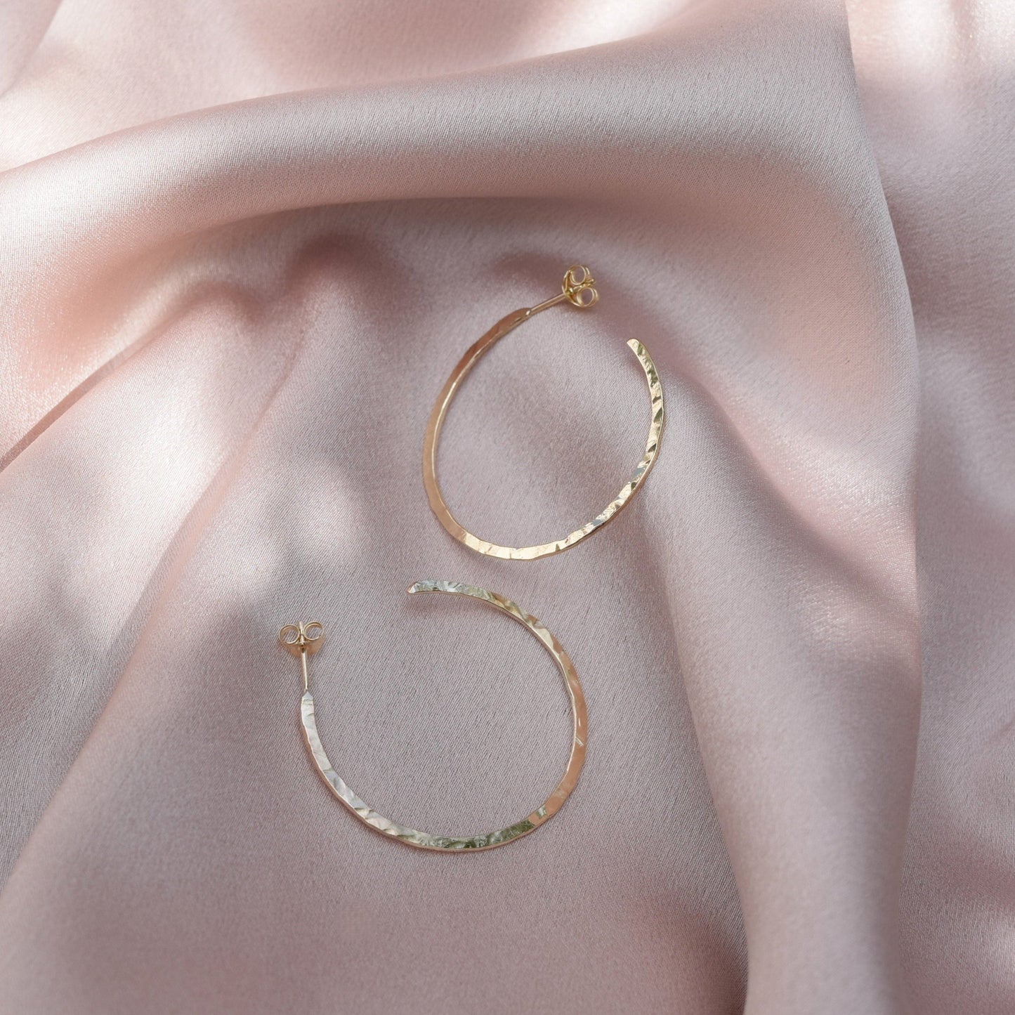 solid 9ct gold hoop earrings laying on a blush pink fabric background