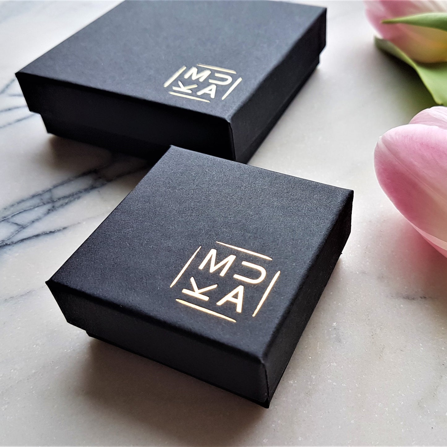 Image of MUKA branded gift boxes that come with earrings. Matt black FSC certified cardboard boxes with MUKA logo embossed in gold in bottom right corner