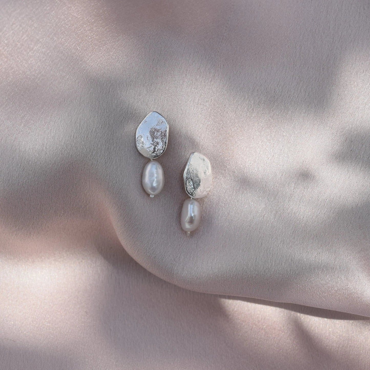 Silver Bella pearl earrings hanging from blush pink silk fabric