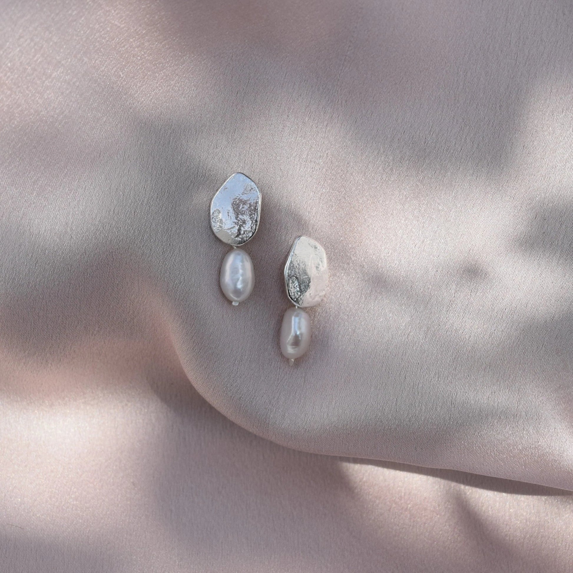 Silver Bella pearl earrings hanging from blush pink silk fabric