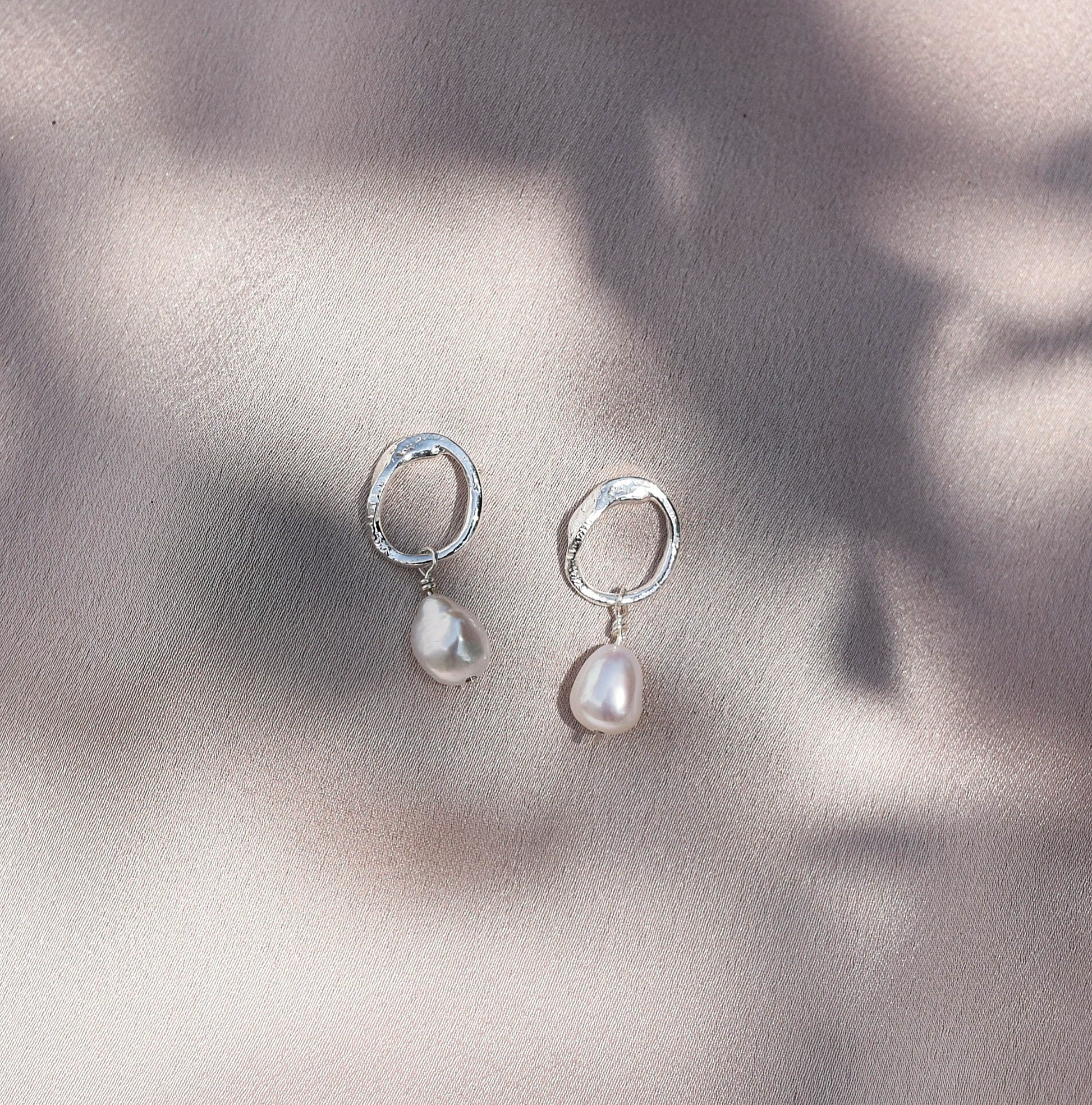 Grace earrings shinning in the sun on a pale pink background