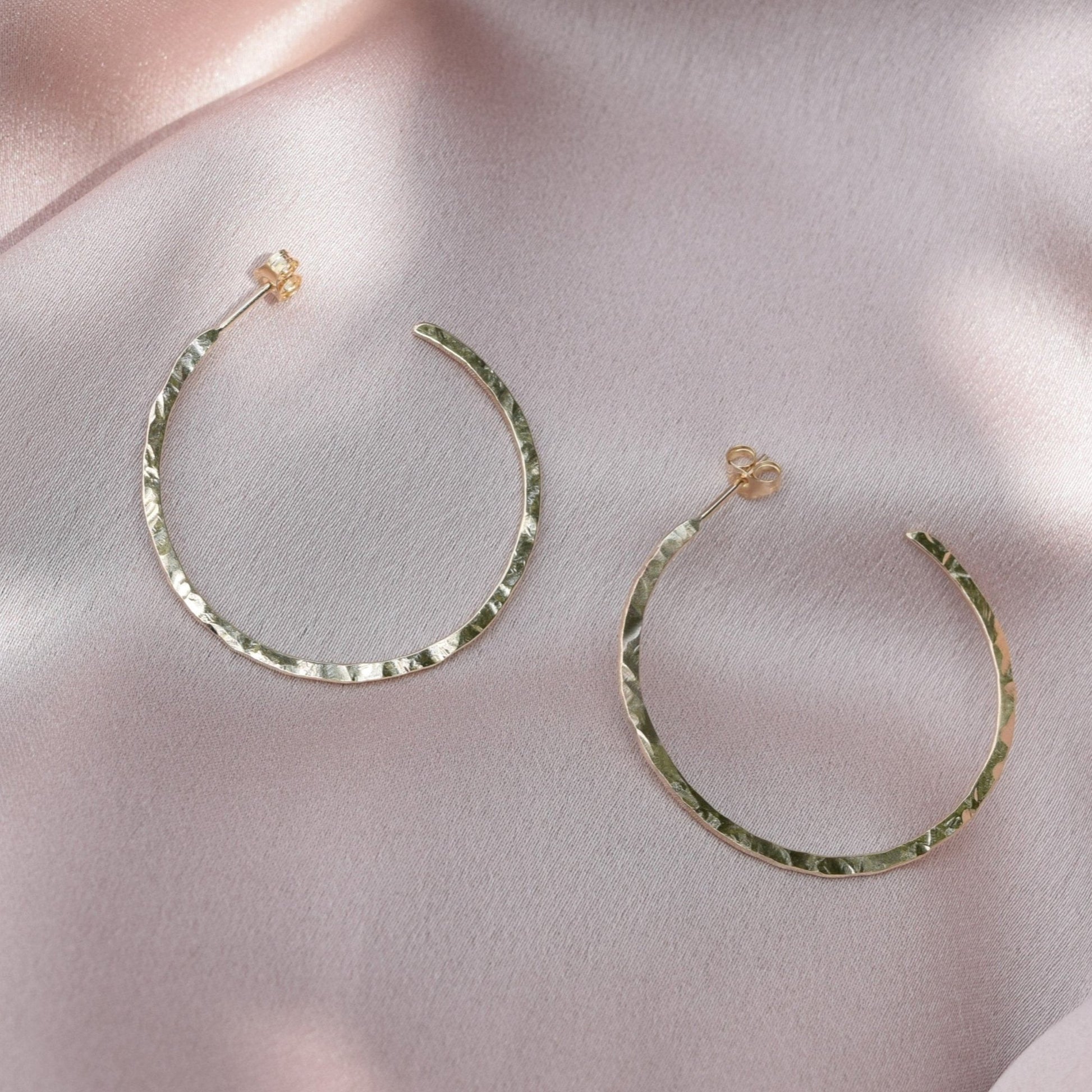 solid 9ct gold hoop earrings laying on a blush pink fabric background