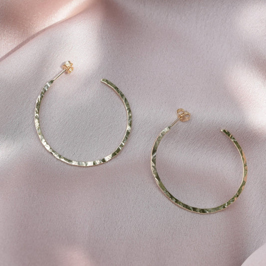 solid 9ct gold hoop earrings laying on a blush pink fabric background