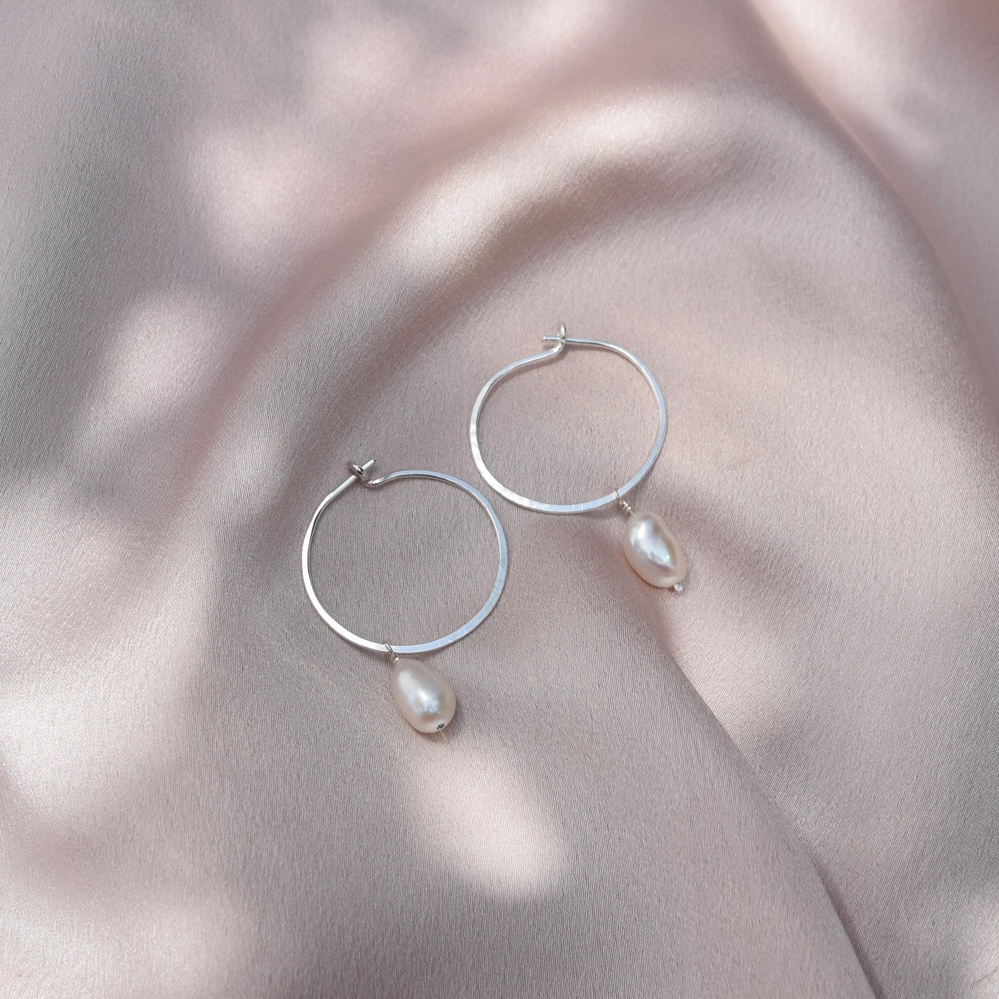 sterling silver pearl hoops laying on silk fabric