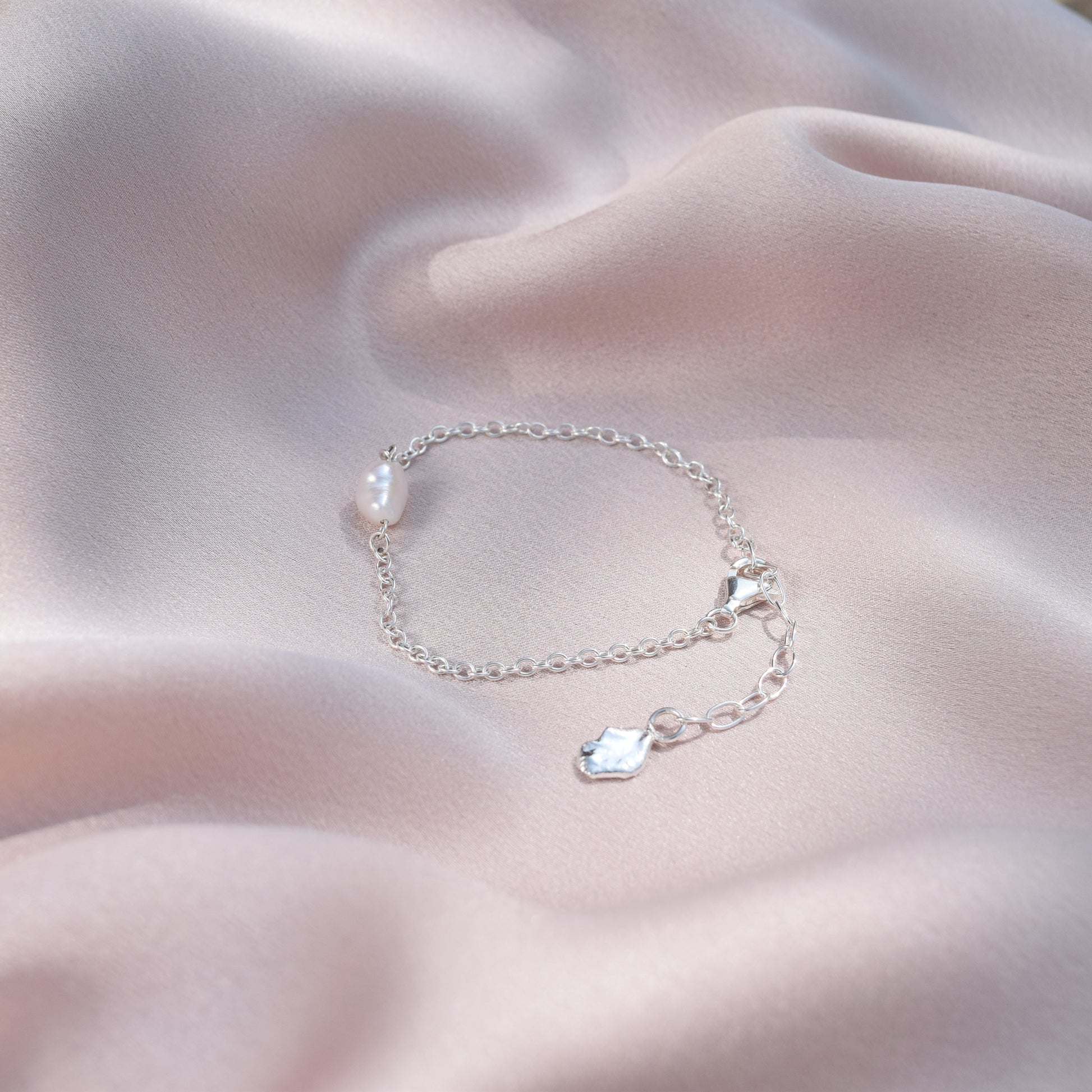 sterling silver pearl bracelet laying on a blush coloured silk background