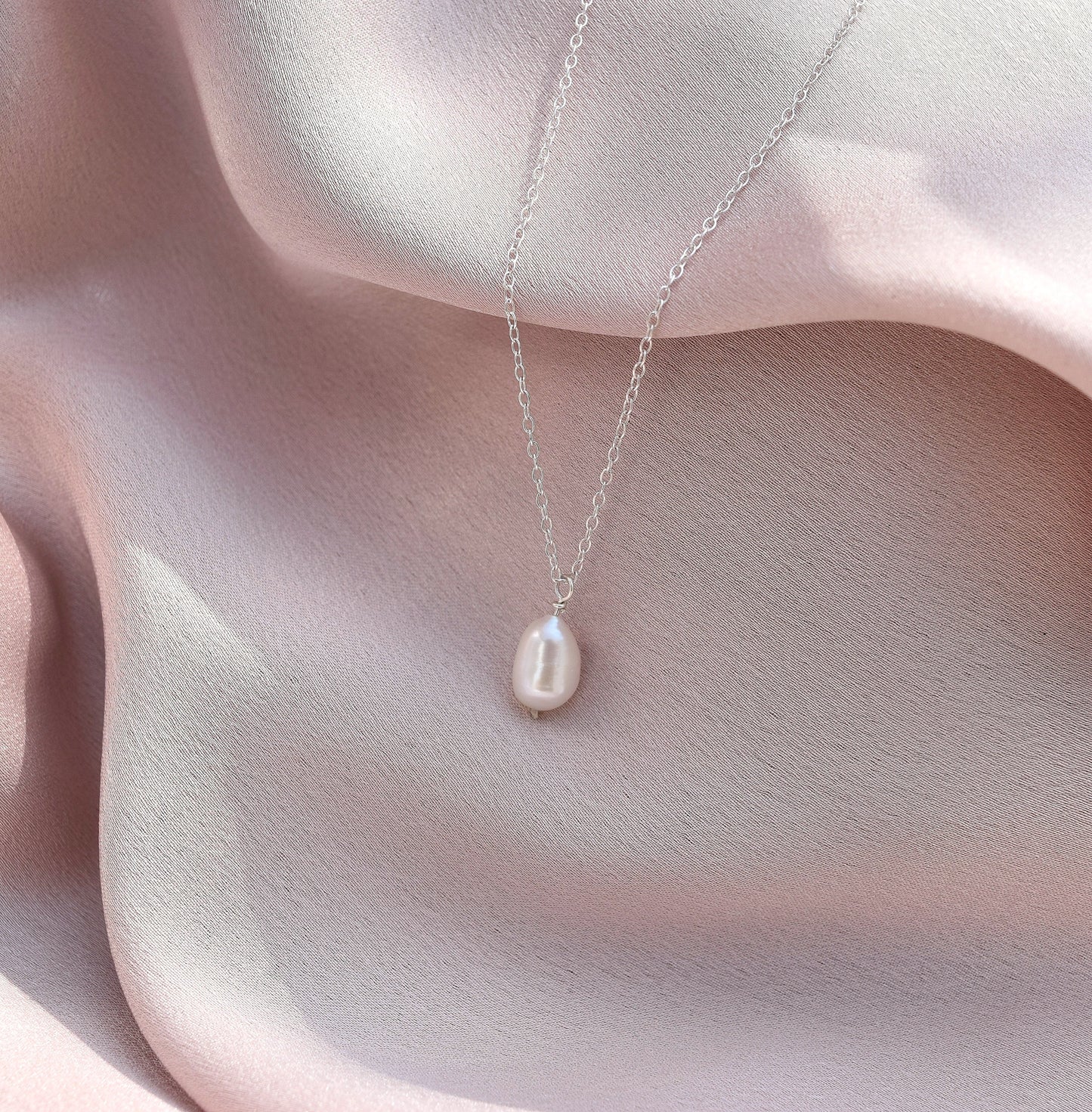 silver pearl necklace laying on silk fabric