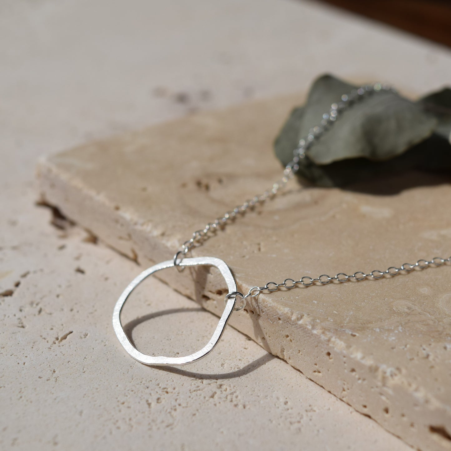 silver organic shape necklace laying on stone in sunlight