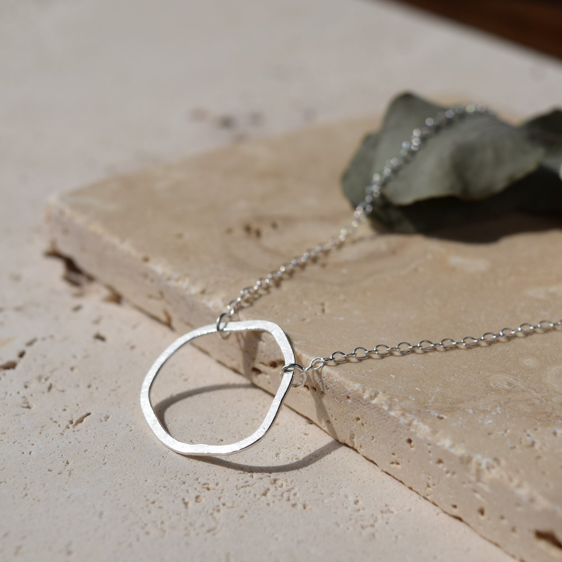 silver organic shape necklace laying on stone in sunlight