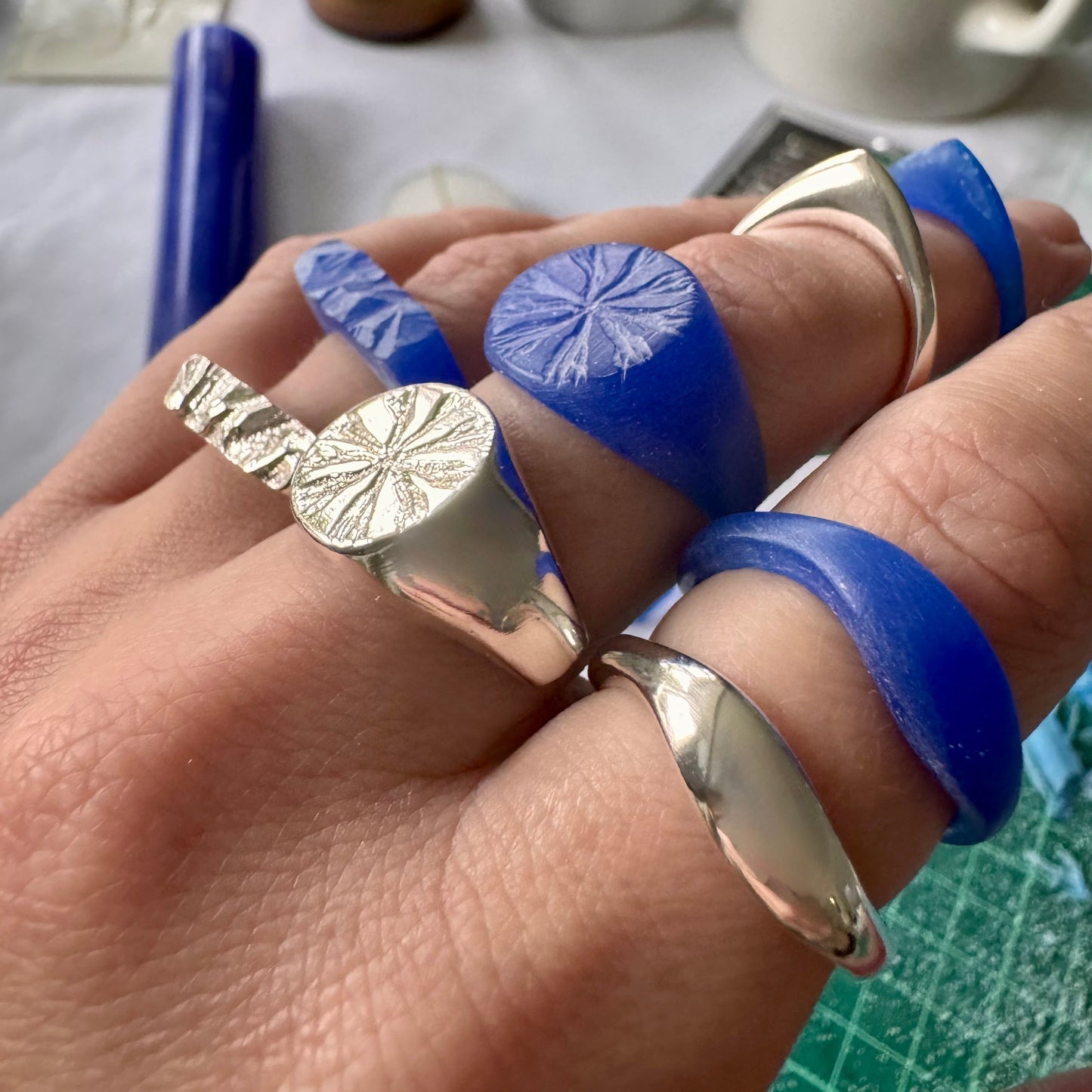 Hand wearing rings - the original blue wax carved ring next to its silver version once it has been cast in sterling silver