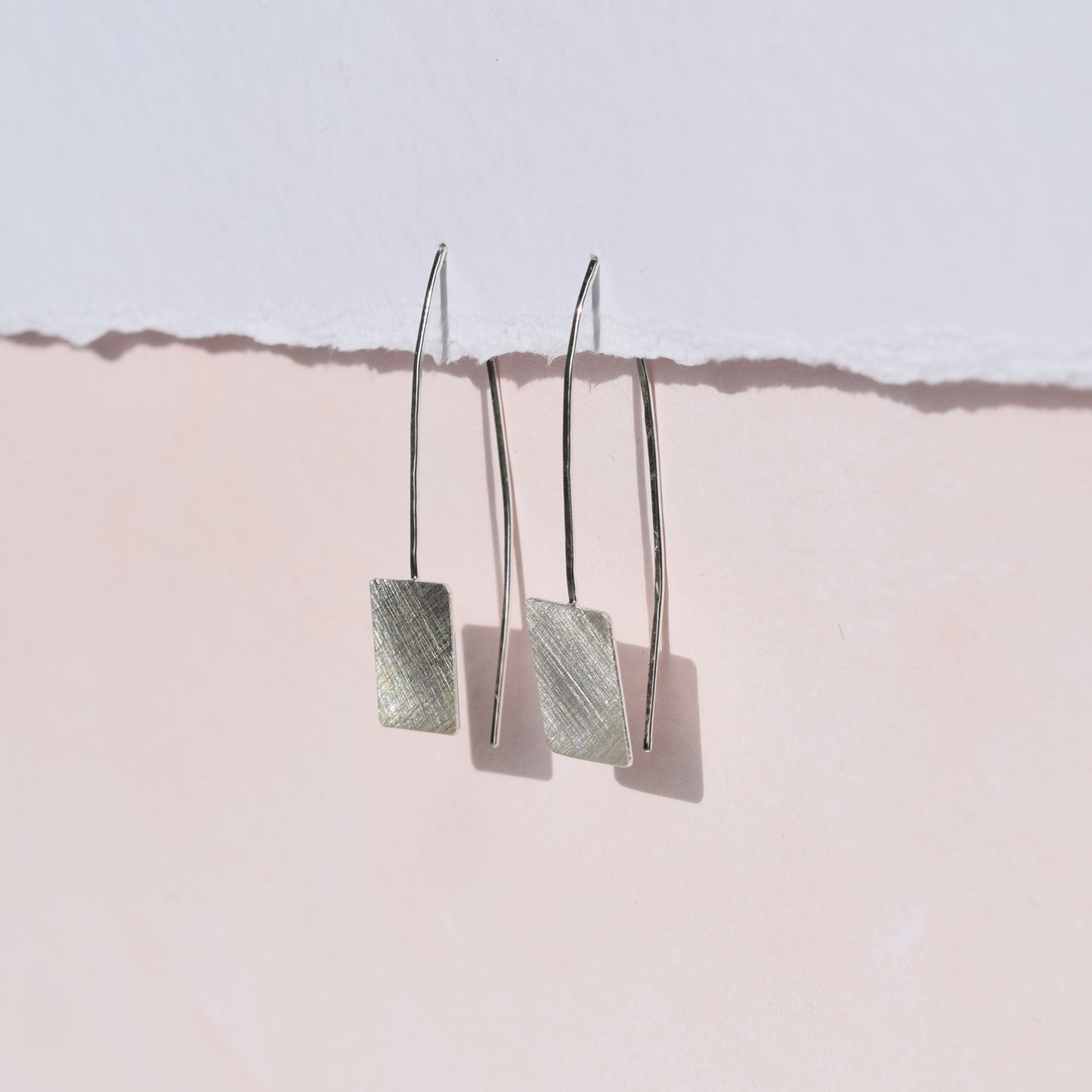 Square drop earrings on pink and white background