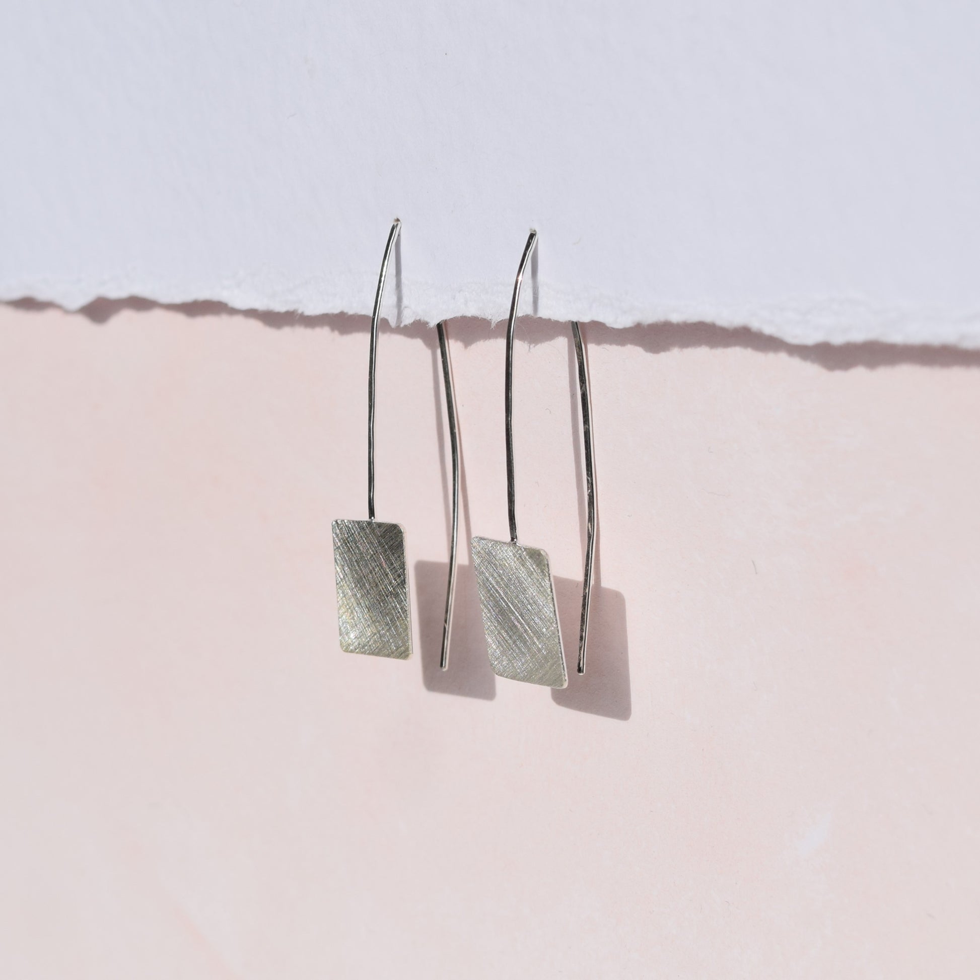 Square drop earrings on pink and white background