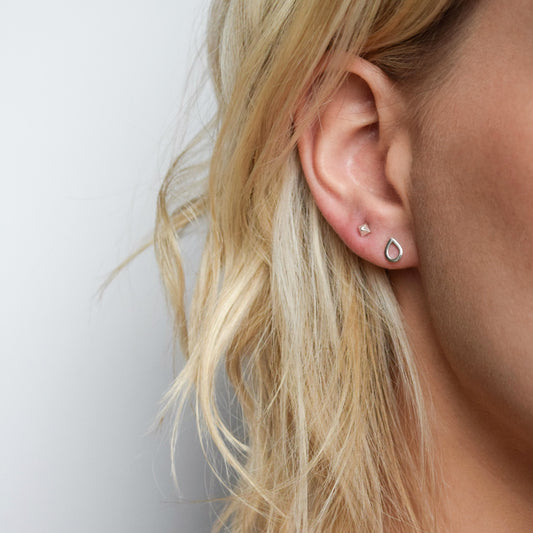 Silver teardrop stud earrings worn alongside pyramid stud