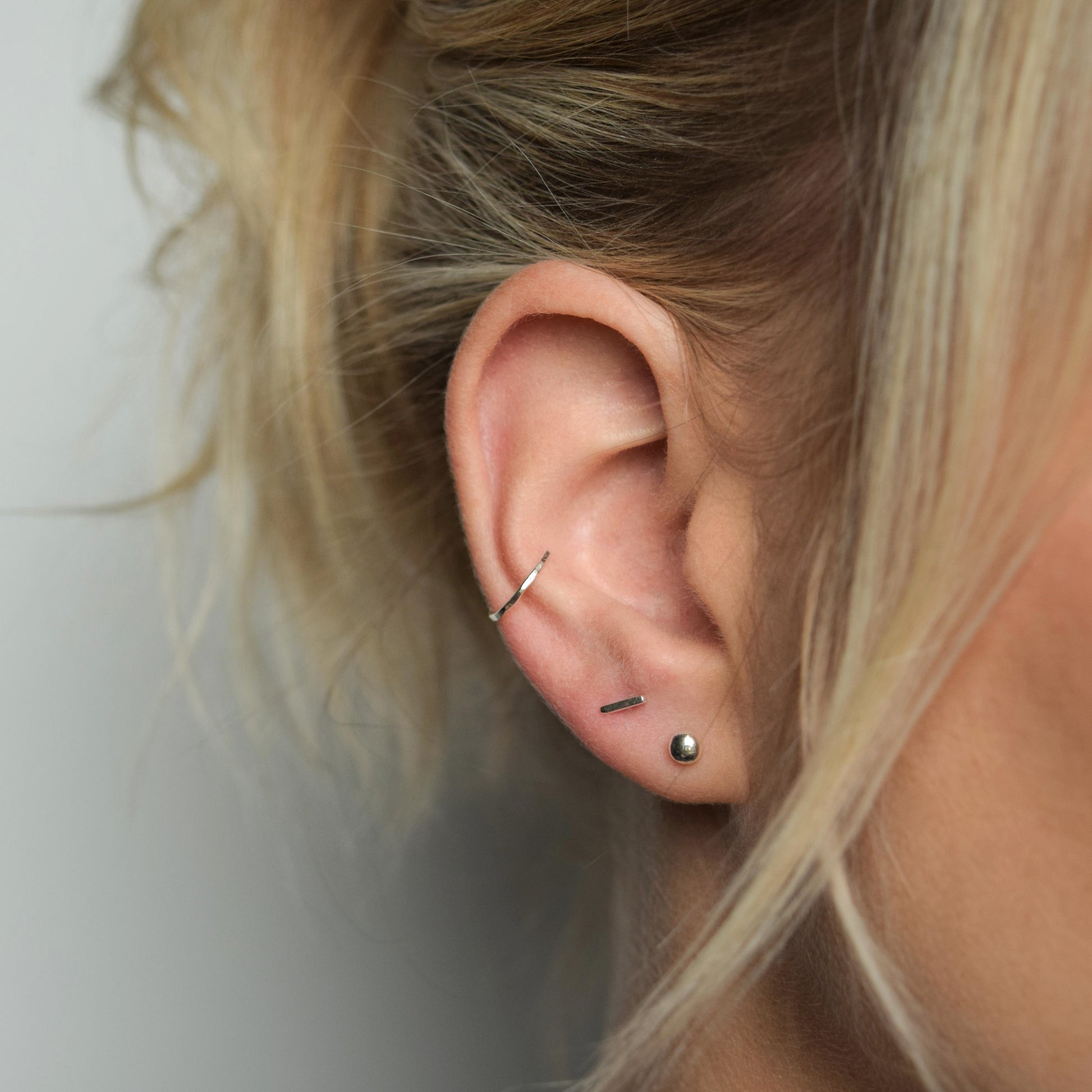 silver conch cuff worn alongside bar studs and organic ball studs