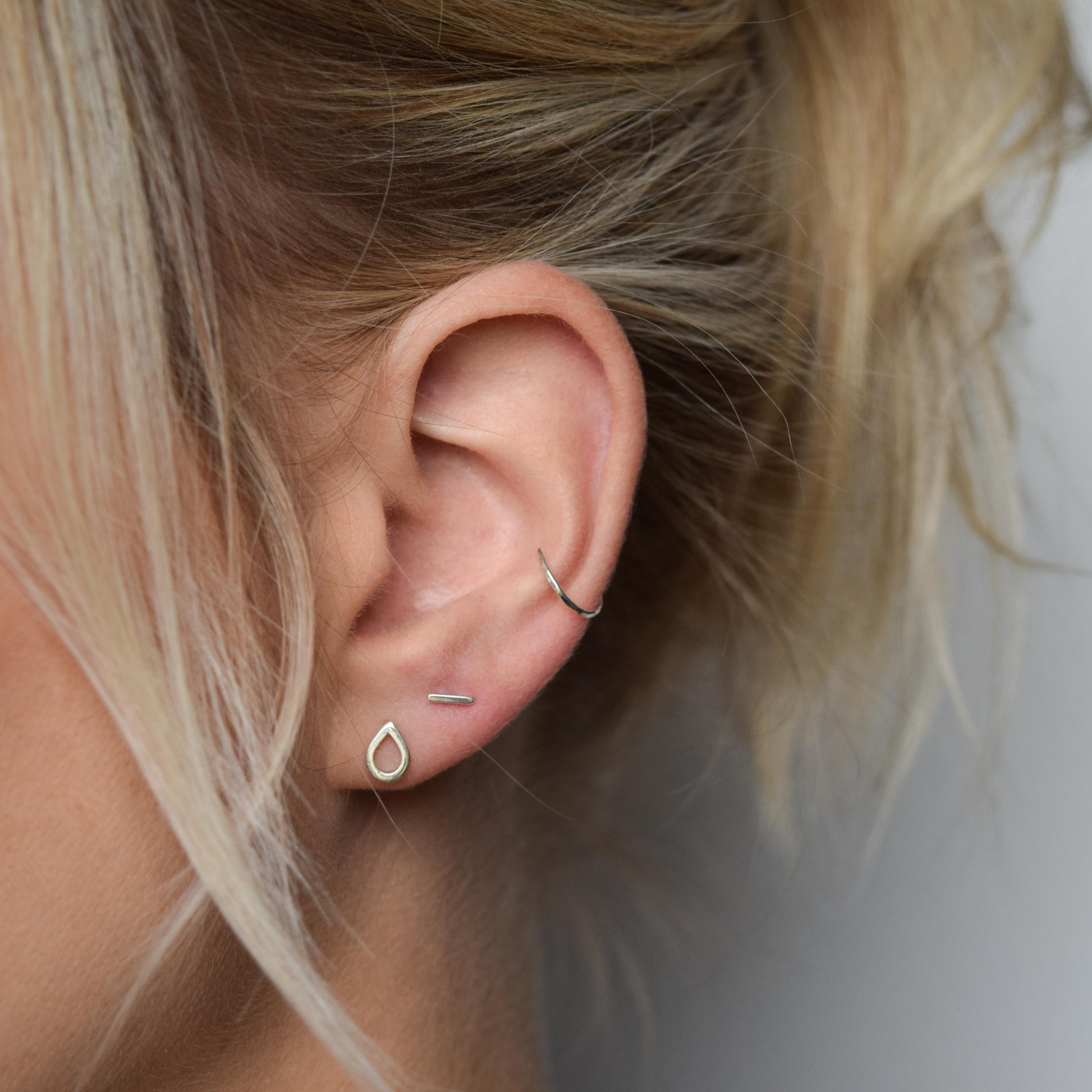 silver conch cuff worn alongside teardrop studs and bar studs