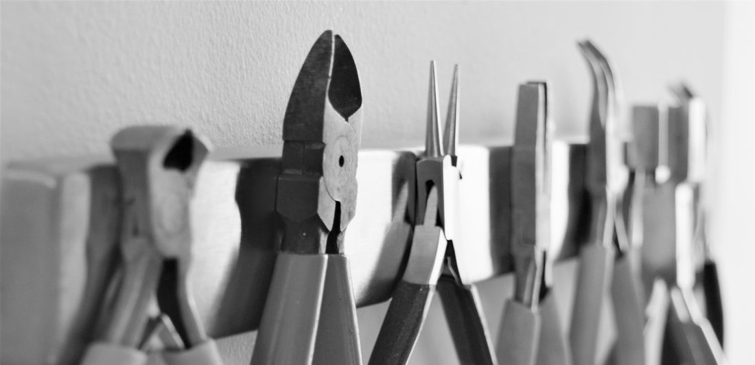 Different types of pliers used in jewellery making lined up on a magnetic strip on the wall