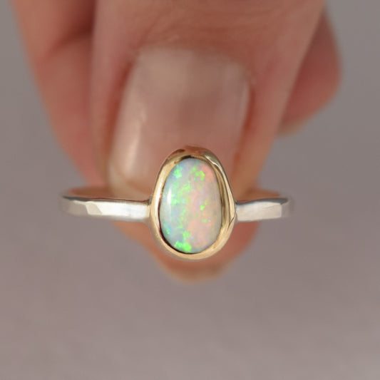 Gold and silver ring with an opal stone on a neutral background