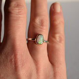 Hand wearing a ring with an opal stone on a neutral background