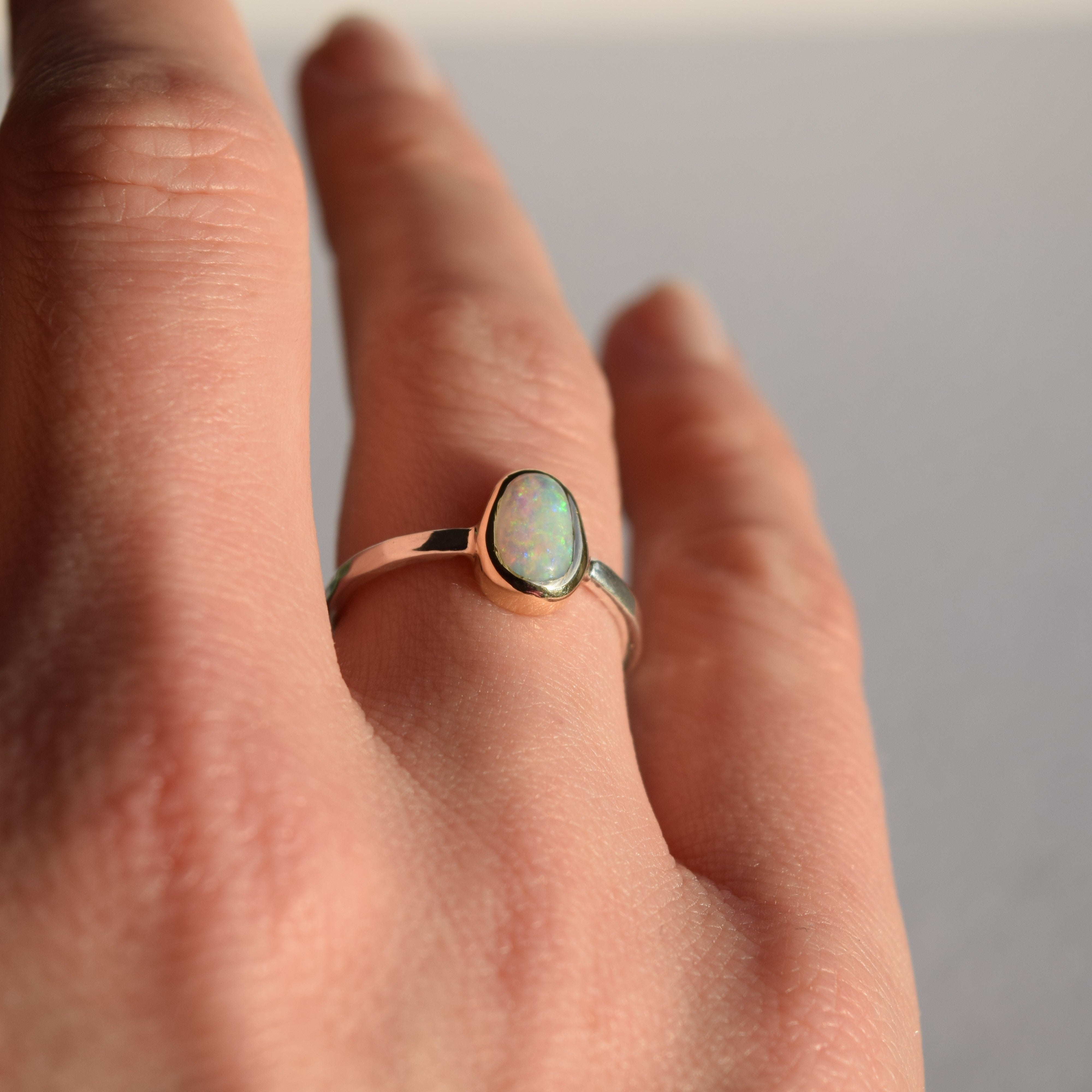 Hand wearing a ring with an opal stone on a neutral background