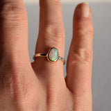 Close-up of a hand wearing an opal ring with a plain background