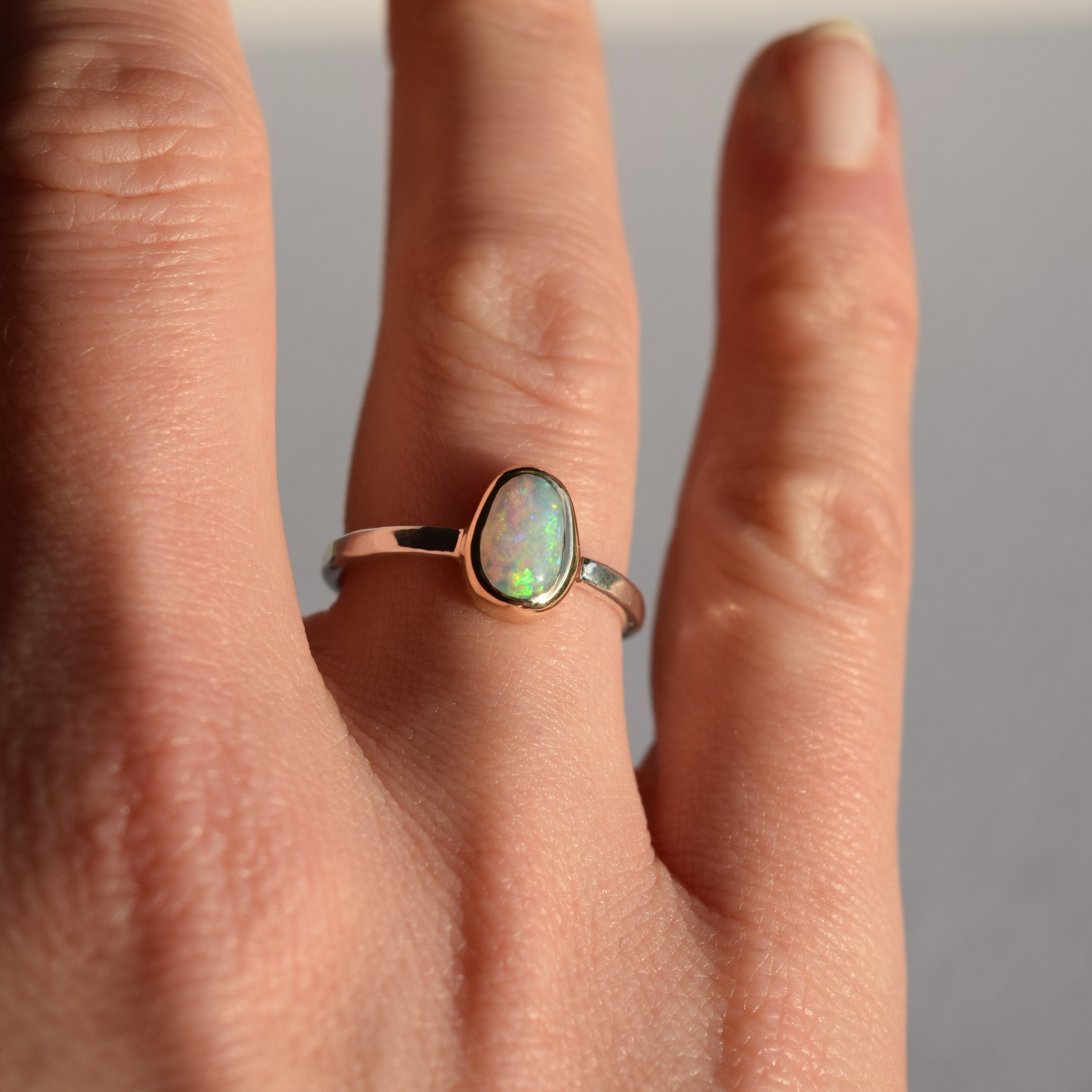 Close-up of a hand wearing an opal ring with a plain background