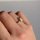 Hand wearing a ring with a green gemstone on a neutral background