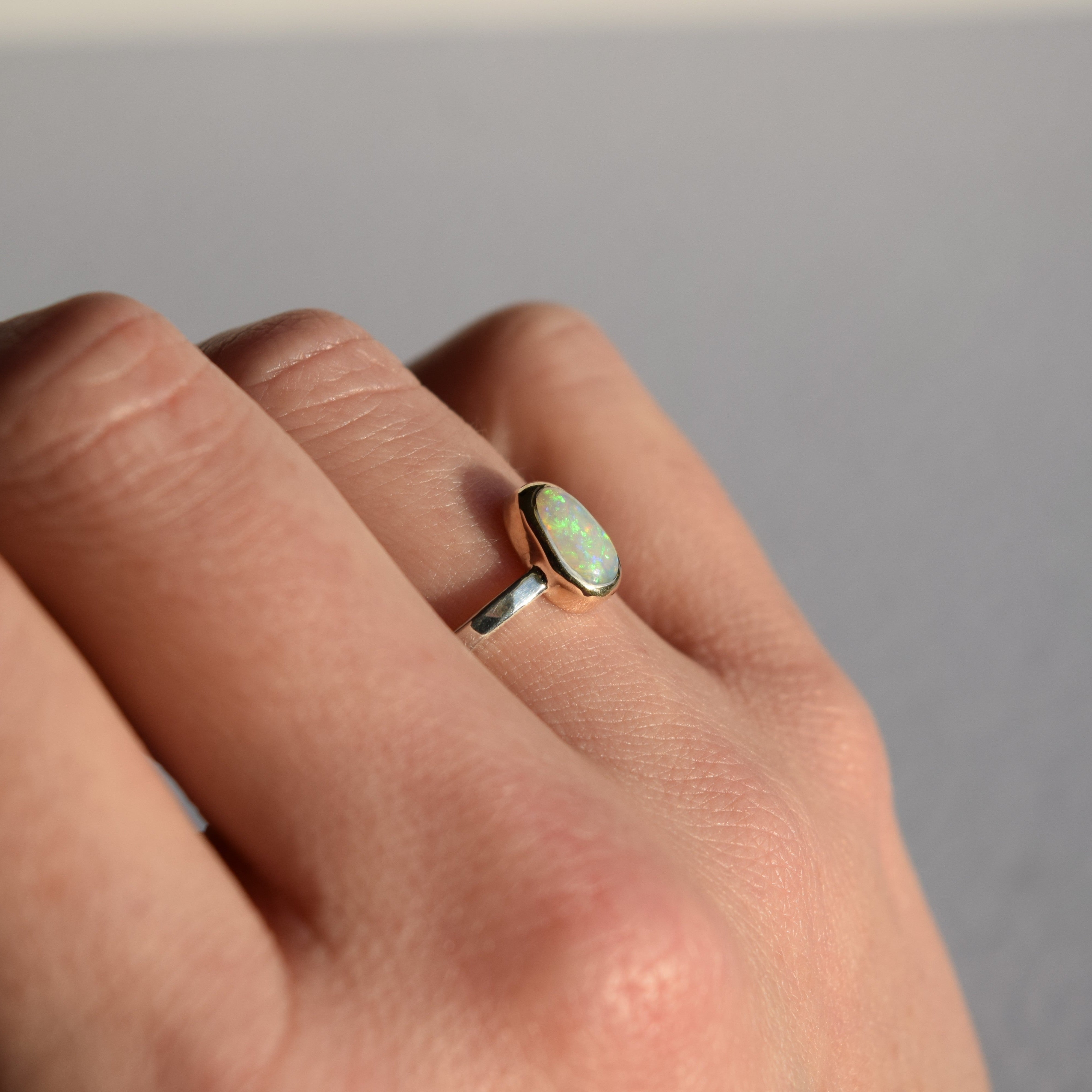 Hand wearing a ring with a green gemstone on a neutral background