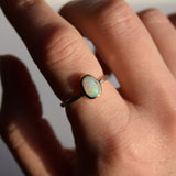 Close-up of a hand wearing a ring with an opal stone on a neutral background