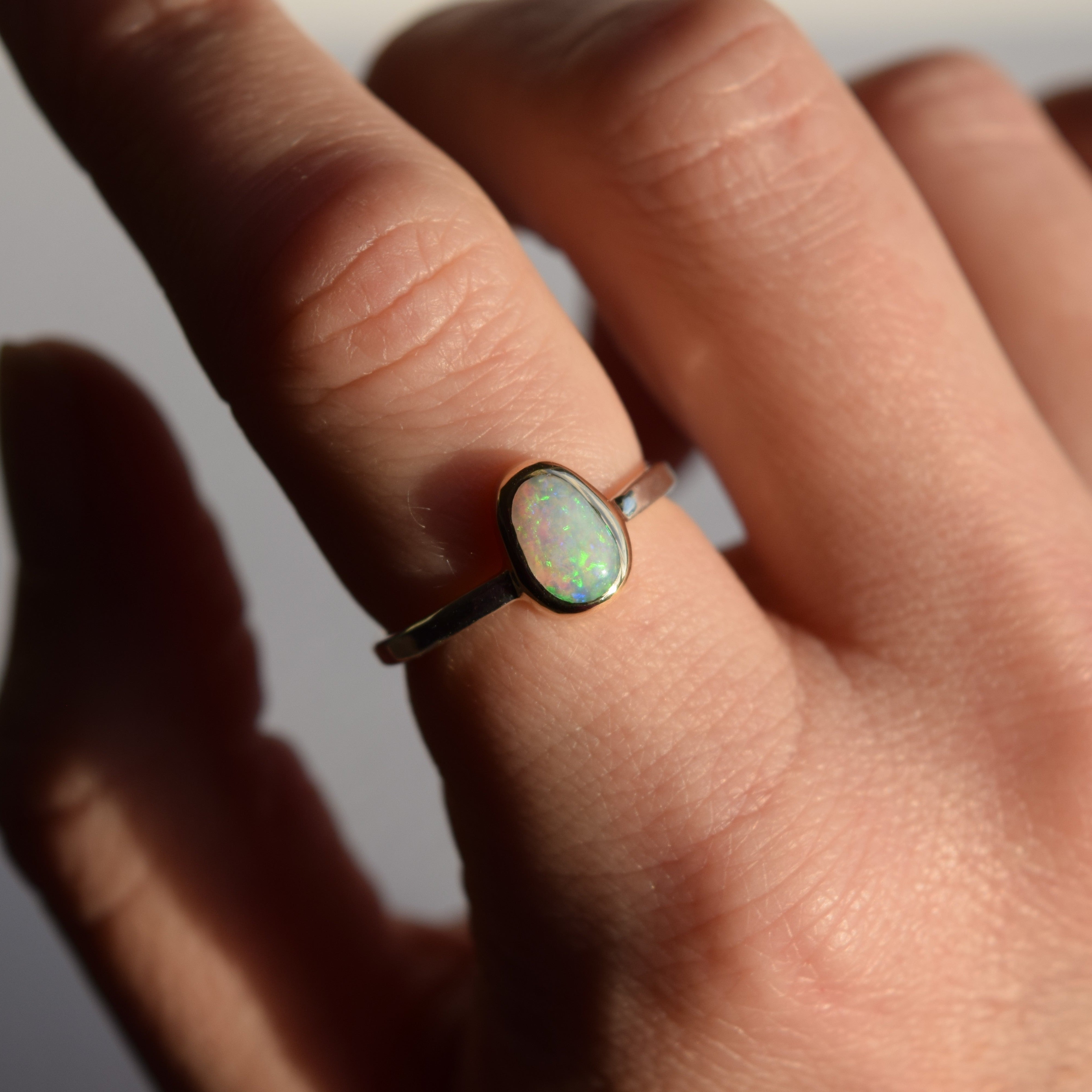 Close-up of a hand wearing a ring with an opal stone on a neutral background