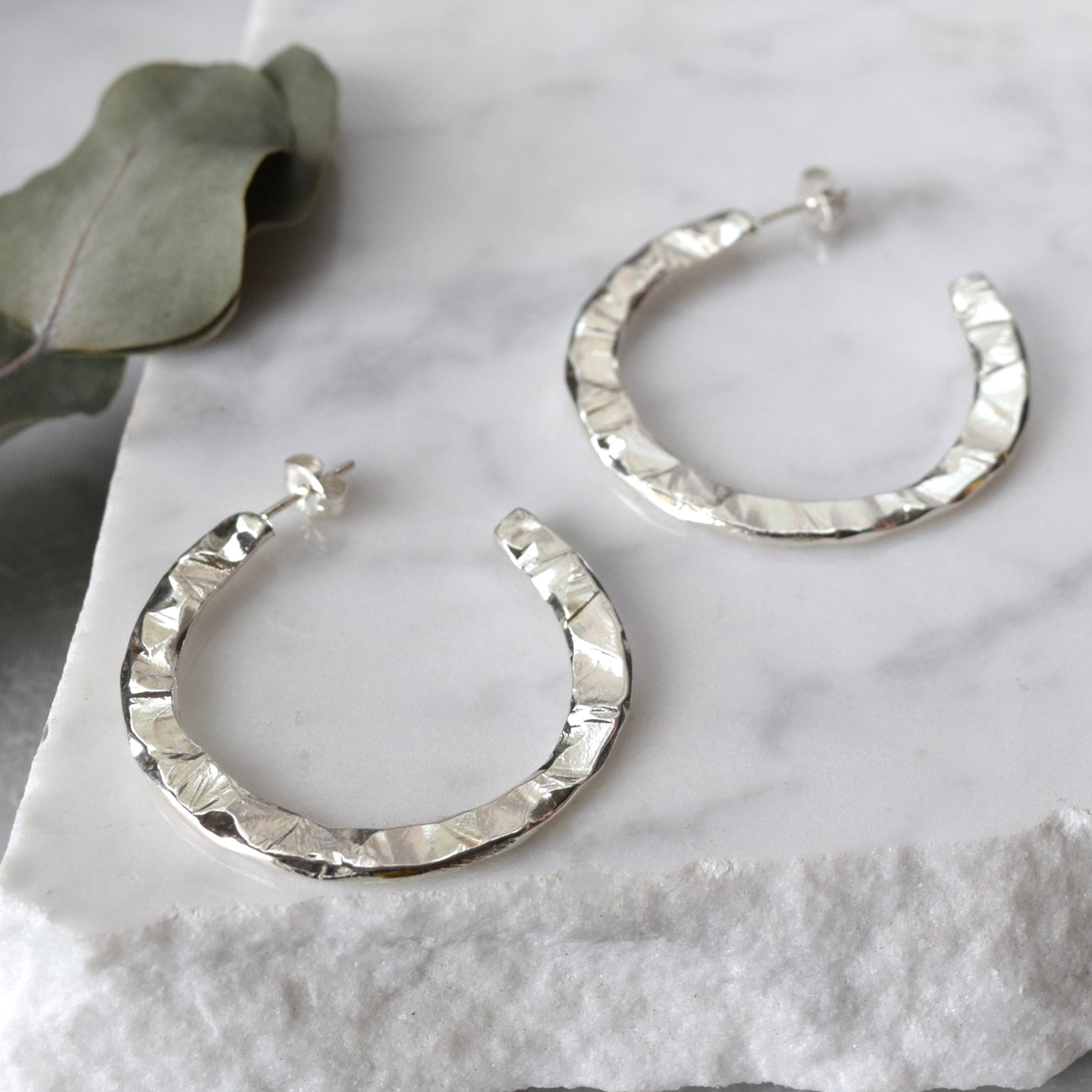 Product image of the Cosmo hoops earrings in silver showing the carved texture on the earrings