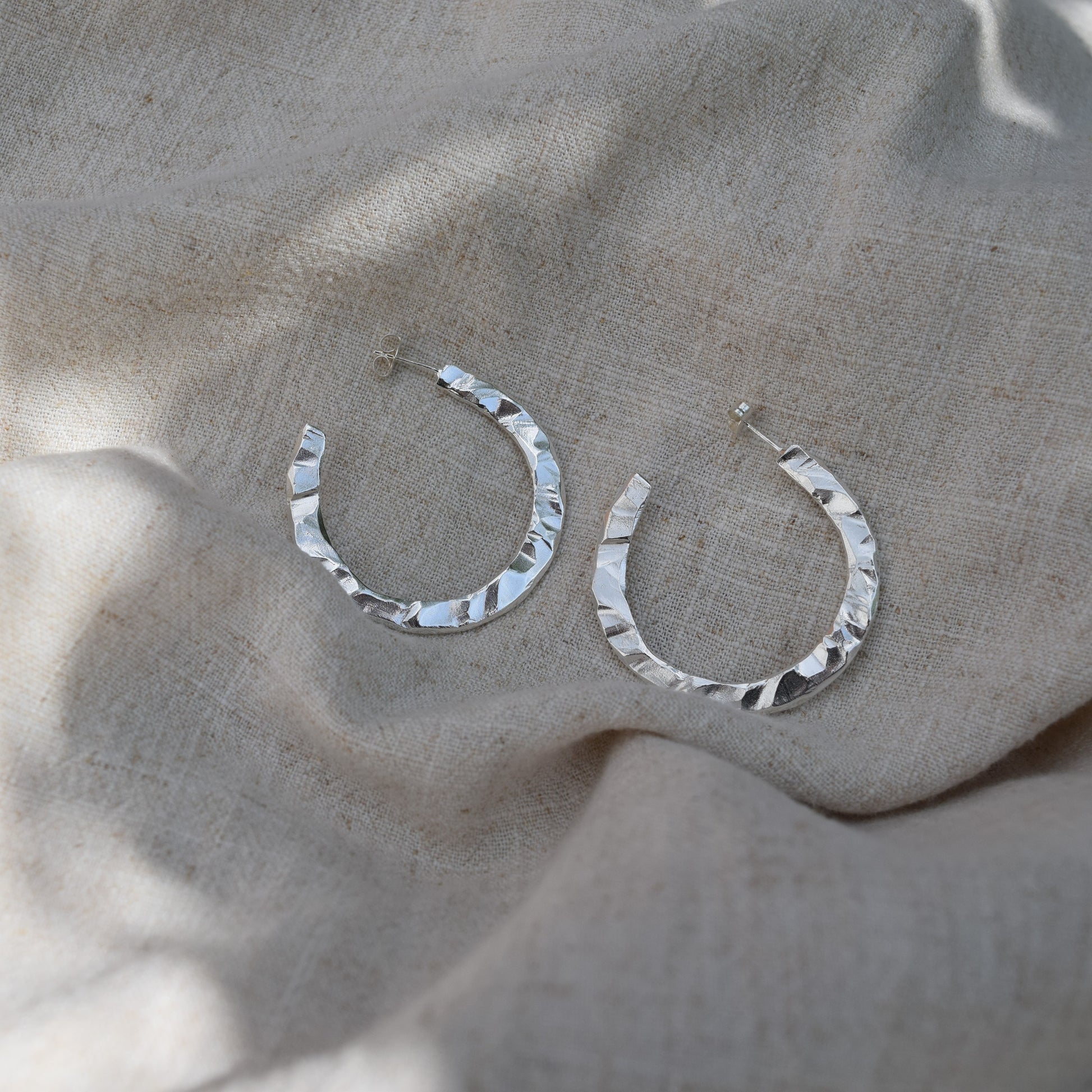 Image of silver Cosmo hoops on natural fabric