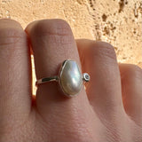 Silver ring with a large pearl stone and diamond on a finger against a beige background