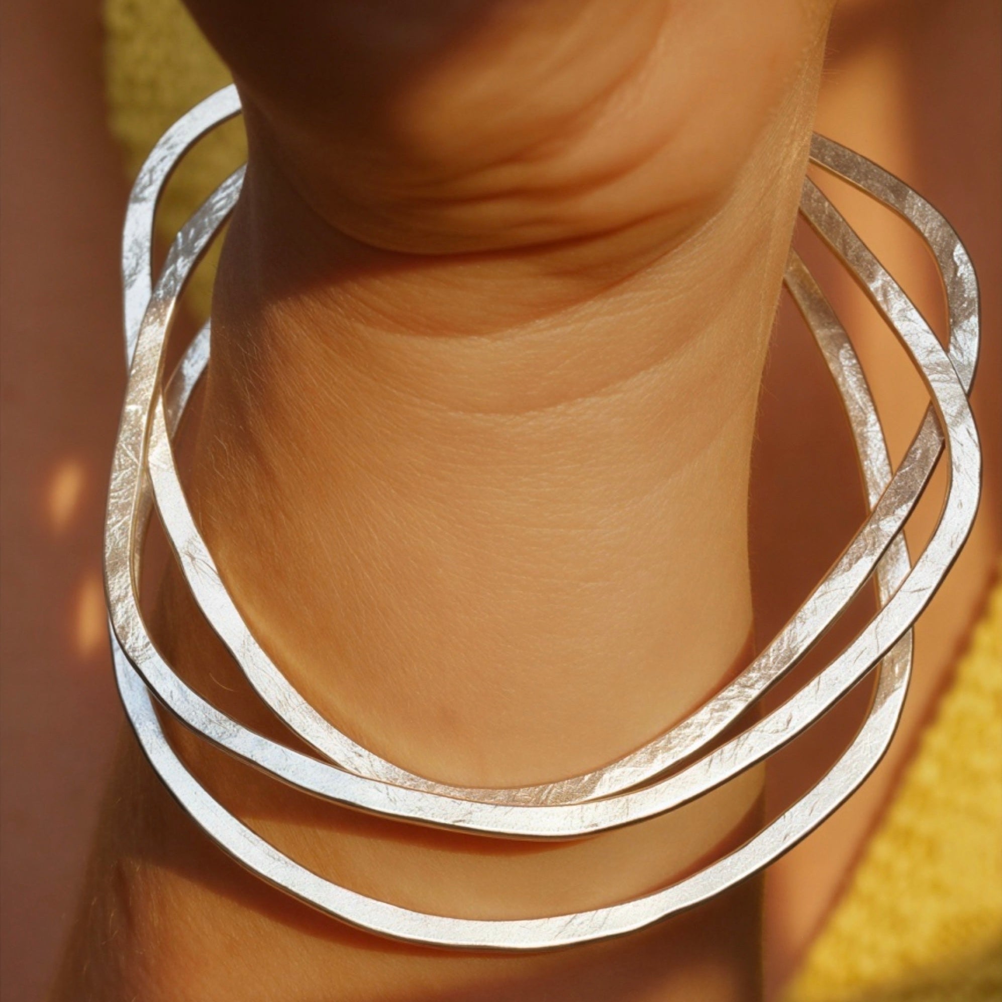 A close-up of a person's wrist wearing three overlapping hammered silver bangles.