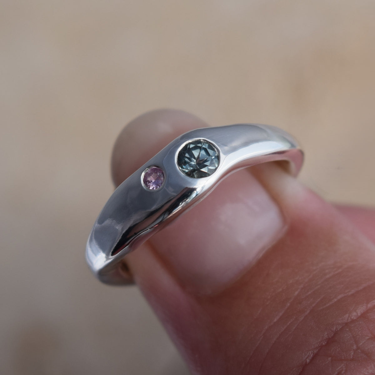 Wave molten effect silver ring with two sapphires flush set into the silver - a large aqua blue sapphire and a smaller pink sapphire