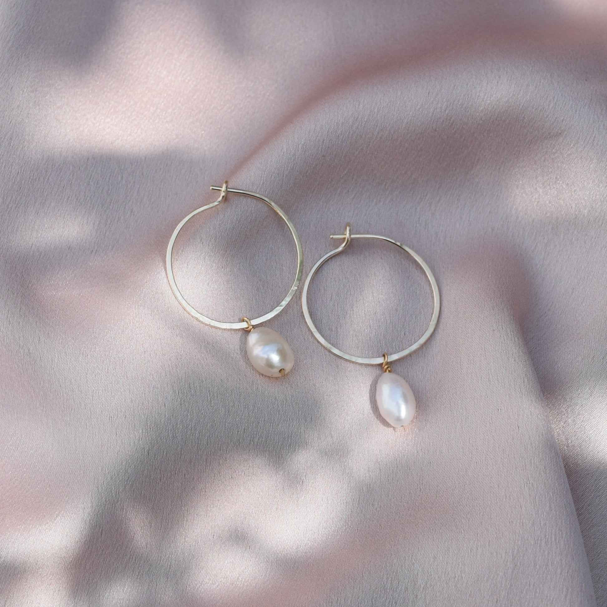 gold hoops with a keshi pearl hanging from them laying on silk fabric