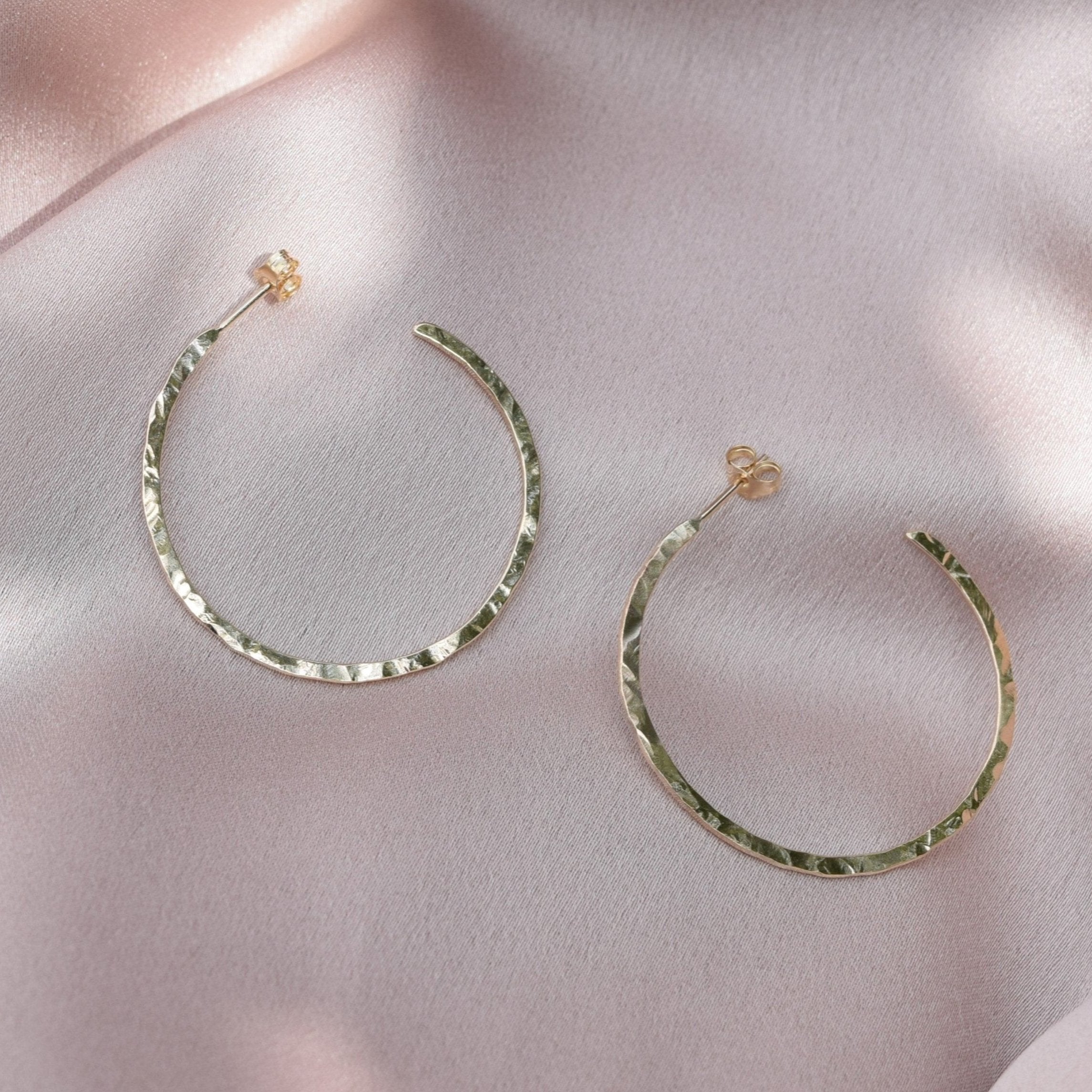 solid 9ct gold hoop earrings laying on a blush pink fabric background