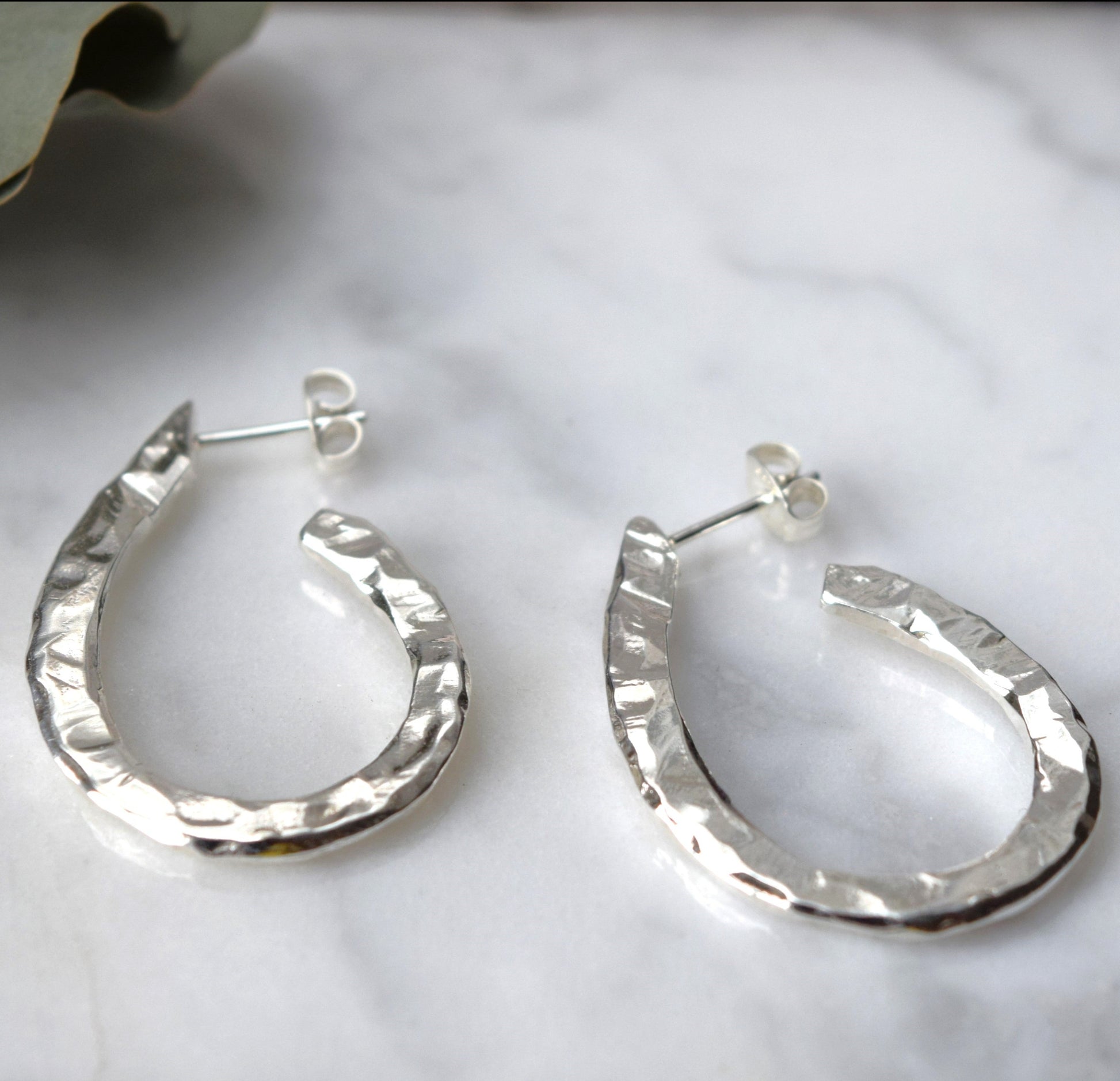 Carved oval hoop earrings resting against a stone on a white background with a mirror reflection in the background
