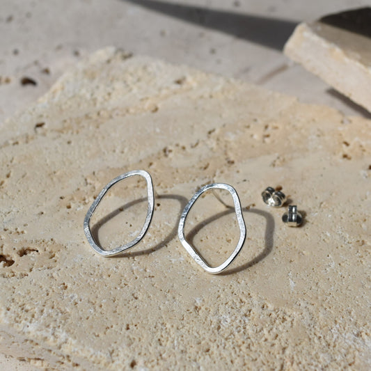 silver organic shape earrings sitting on a stone in the sunlight