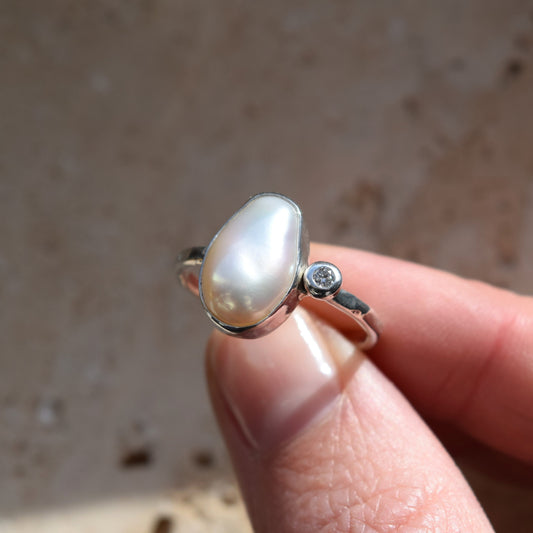 Pearl ring with a diamond on a finger against a neutral background