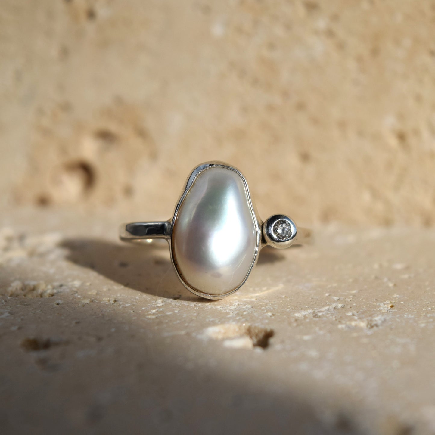 Pearl ring with a diamond on a sandy surface