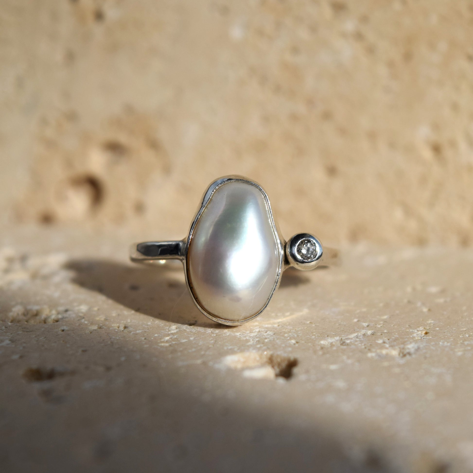 Pearl ring with a diamond on a sandy surface