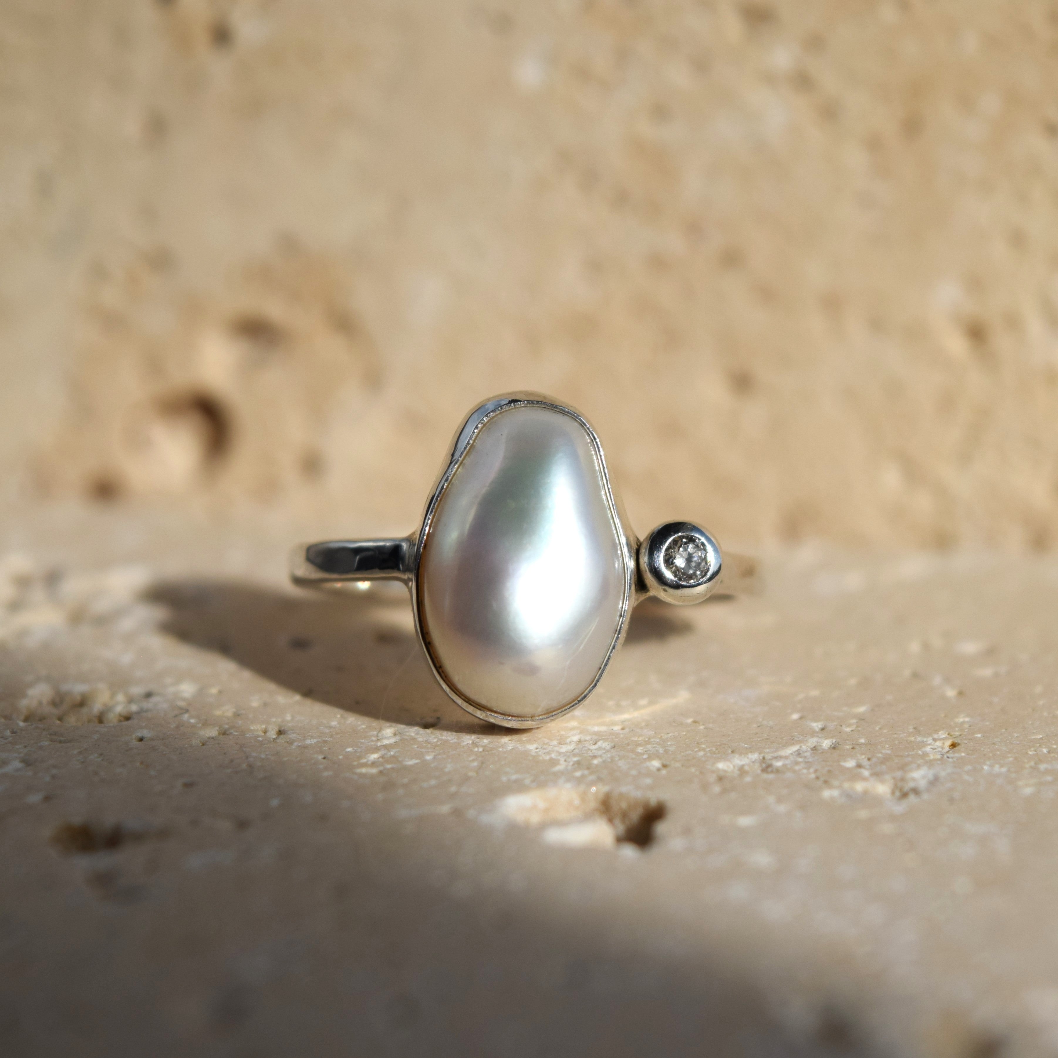 Pearl ring with a diamond on a sandy surface