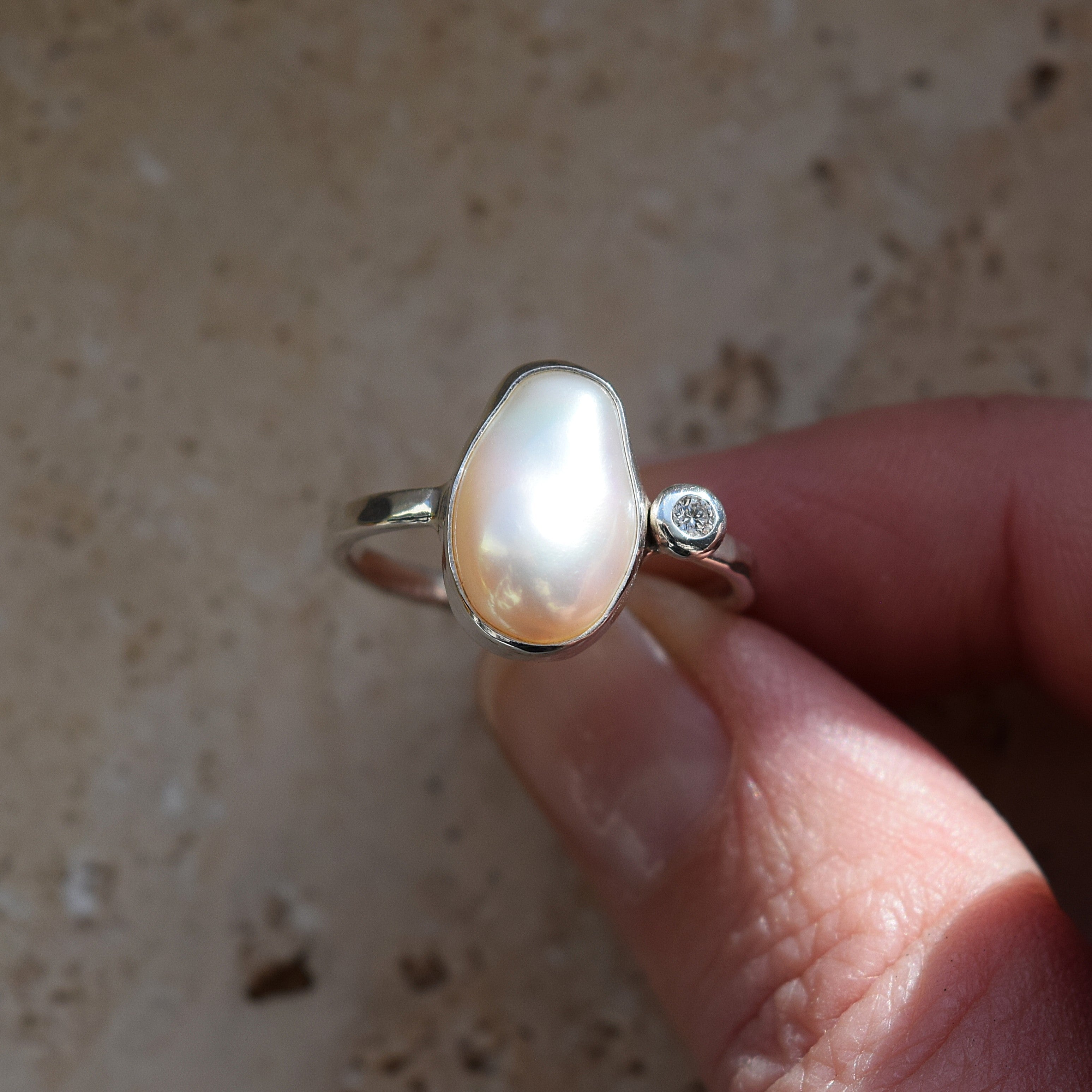 Pearl ring with a diamond on a finger against a neutral background