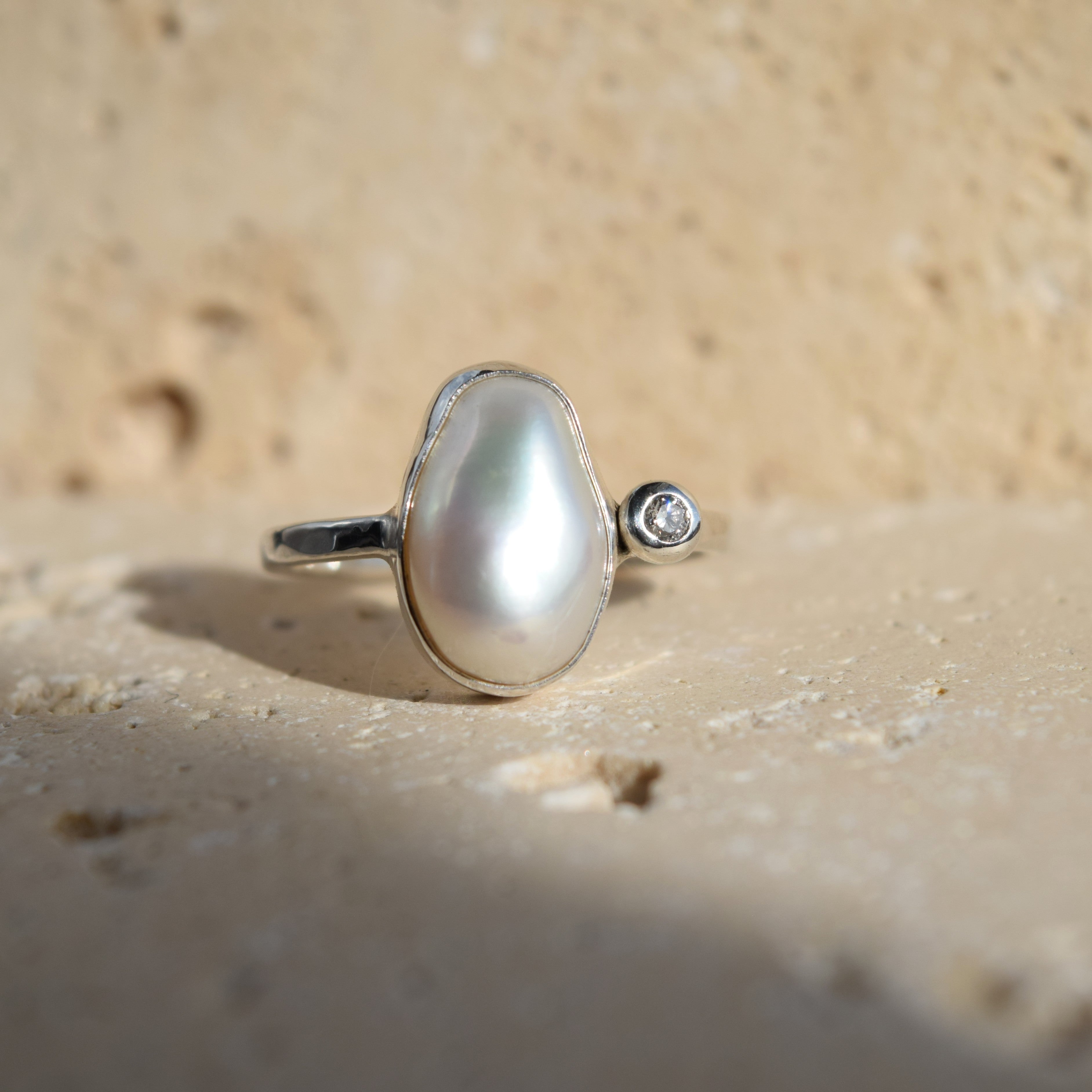 Pearl ring with a diamond on a sandy background