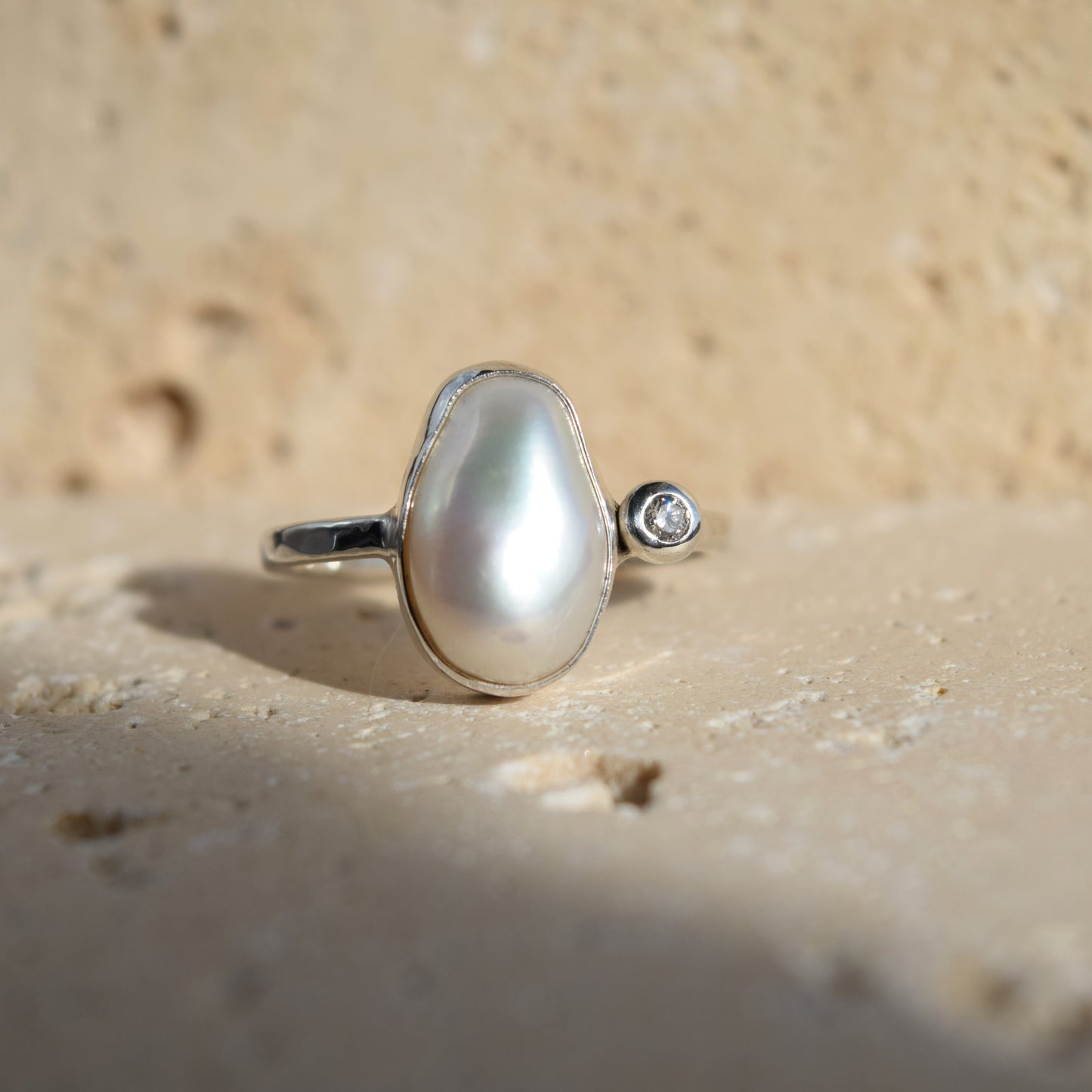 Pearl ring with a diamond on a sandy background