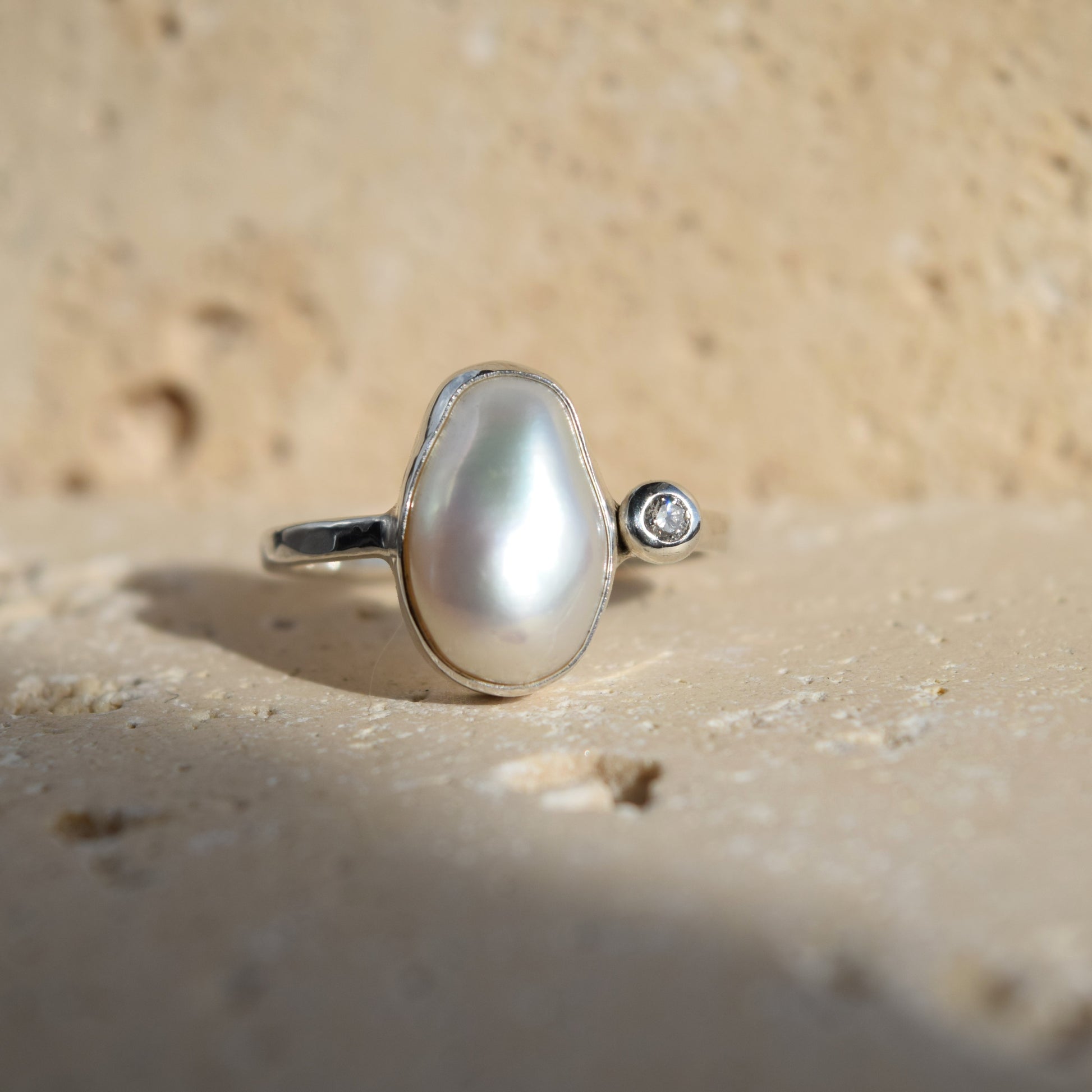 Pearl ring with a diamond on a sandy background