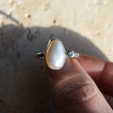 Pearl ring with a diamond on a finger against a blurred background