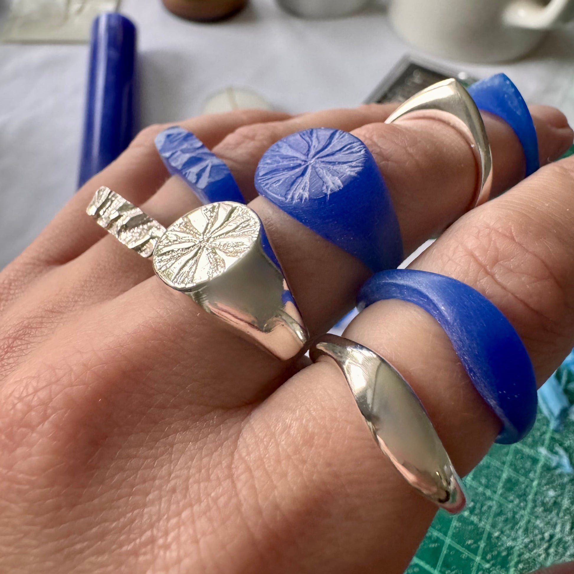 Hand wearing rings - the original blue wax carved ring next to its silver version once it has been cast in sterling silver