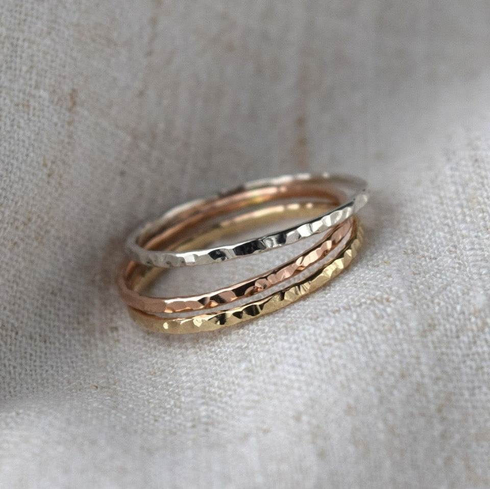 Three rings with hammered finish held in fabric. Rings are made in sterling silver, 9ct gold and 9ct rose gold
