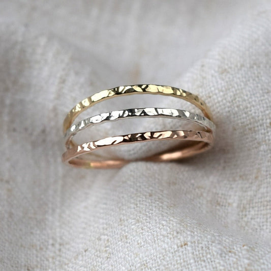 Three rings with hammered finish held in fabric. Rings are made in sterling silver, 9ct gold and 9ct rose gold